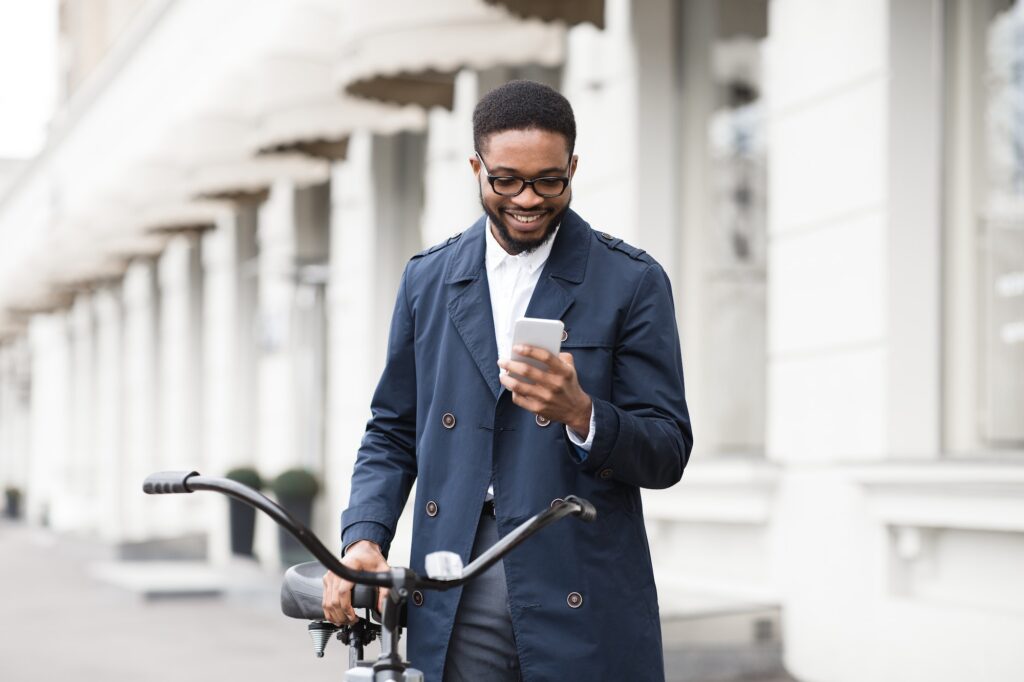 Way to work. Man texting on phone, standing with bike